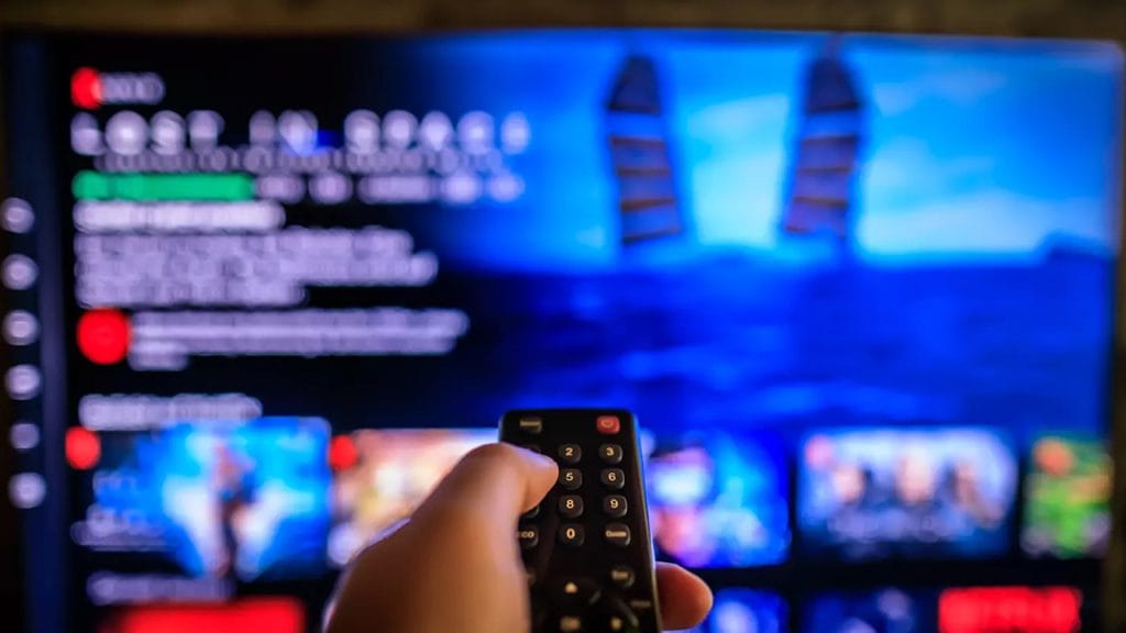 A hand with a remote control pointing towards a smart TV. Movies and series in English also help you learn English fast.